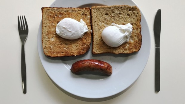Two pieces of toast on a white plate with poached eggs and piece of toast, resembling a sad face.